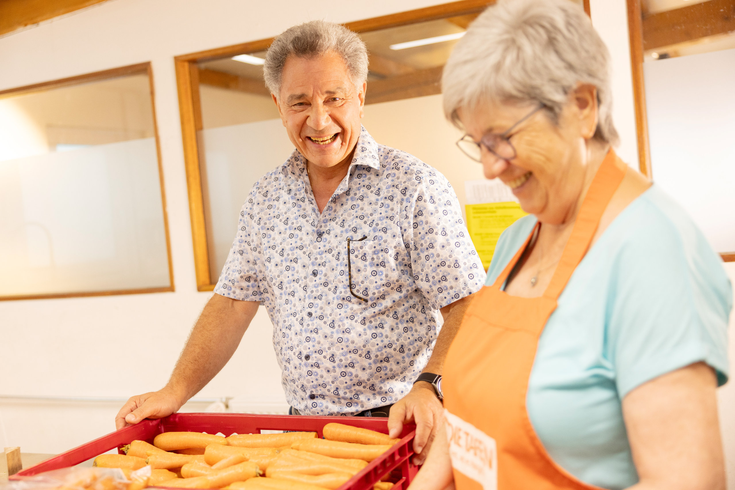 Ein lachender Mann und eine ehrenamtliche Helferin der Tettnanger Tafel im Gespräch, während sie Lebensmittel sortieren