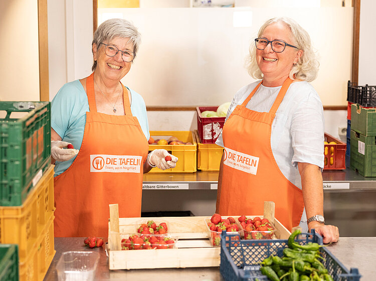 wei Freiwillige der Tettnanger Tafel lächeln, während sie Erdbeeren verpacken