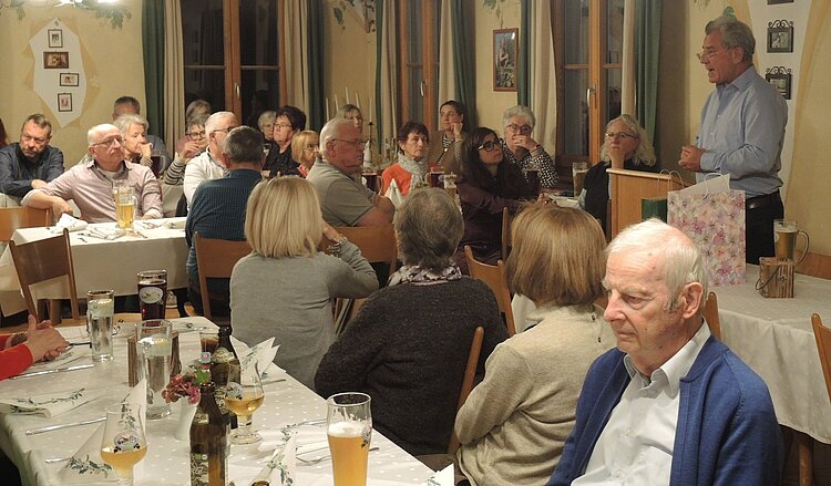 Das Bild zeigt viele Mitarbeitende der Tettnanger Tafel, die gemeinsam am Tisch sitzen. Klaus Nuber, Vorstand, hält eine Ansprache.