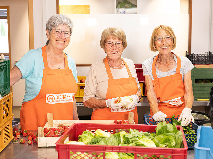Drei Freiwillige der Tettnanger Tafel lächeln, während sie frisches Gemüse sortieren