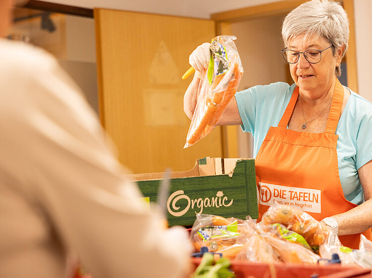 Eine ehrenamtliche Helferin der Tettnanger Tafel, die eine Tüte Karotten an eine Person übergibt