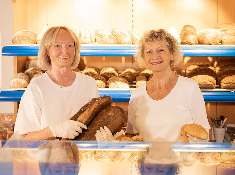 Zwei ehrenamtliche Helferinnen stehen in der Bäckereiabteilung der Tettnanger Tafel und halten frisches Brot in den Händen.